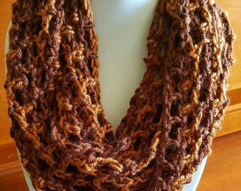 Pode incluir: Uma echarpe infinita de crochê marrom e dourado com uma trama solta e aberta.