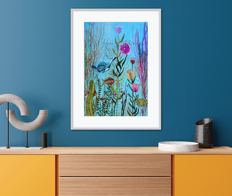 May include: A framed watercolor painting depicting a vibrant underwater scene with colorful flowers, green plants, and blue and orange fish. The background is a light blue color.