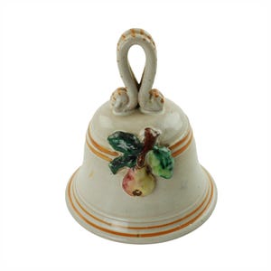 May include: A white ceramic bell with a pear and leaf design. The bell has a brown handle and a gold trim.