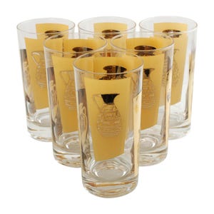 May include: A set of six clear drinking glasses, each featuring a gold and black pitcher design. The glasses have a rectangular gold panel with a detailed pitcher illustration. The glasses are arranged in a circular pattern.