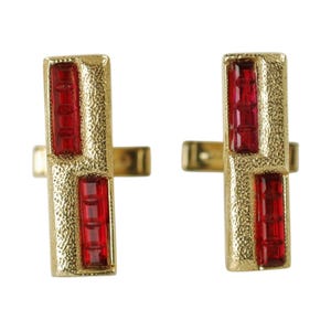May include: A pair of gold-toned cufflinks with a rectangular design. Each cufflink features two sections of rectangular, faceted, red gemstones. The metal has a textured, hammered appearance, and the cufflinks have a classic, elegant style.
