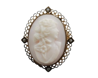 Puede incluir: Un broche de camafeo con un retrato tallado de una mujer en un marco dorado con detalles de perlas.