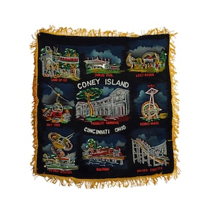 May include: A black velvet pillow with a yellow fringe border features an embroidered illustration of Coney Island amusement park attractions, including the Ferris wheel, roller coaster, and sky ride. The text "Coney Island, Cincinnati Ohio" is embroidered in red and white.