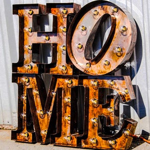 May include: Rustic metal letters spelling "HOME" with light bulbs in each letter. The letters are brown and have a distressed look.
