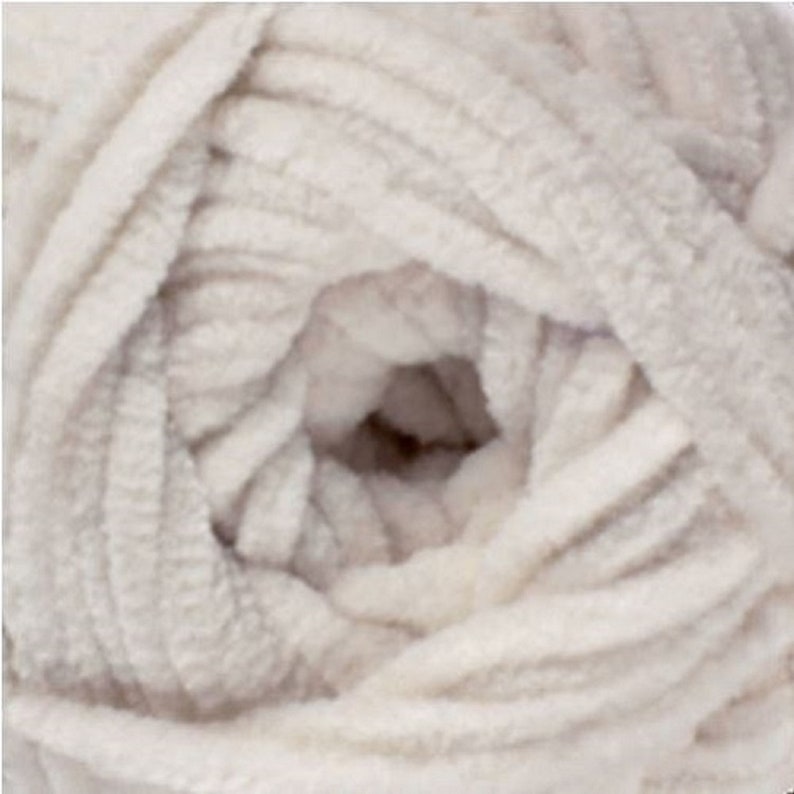 May include: A skein of white yarn with a soft, fuzzy texture. The yarn is tightly wound and has a slightly textured surface.