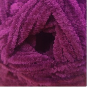 May include: A close-up of a deep purple yarn with a fuzzy texture. The yarn is tightly wound into a ball shape.