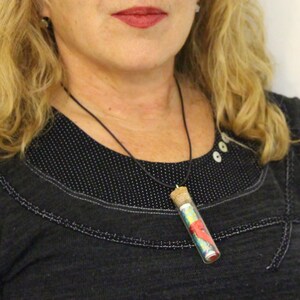May include: A black necklace with a small glass vial pendant filled with colourful fabric scraps. The vial has a cork stopper and is hanging from a black cord.
