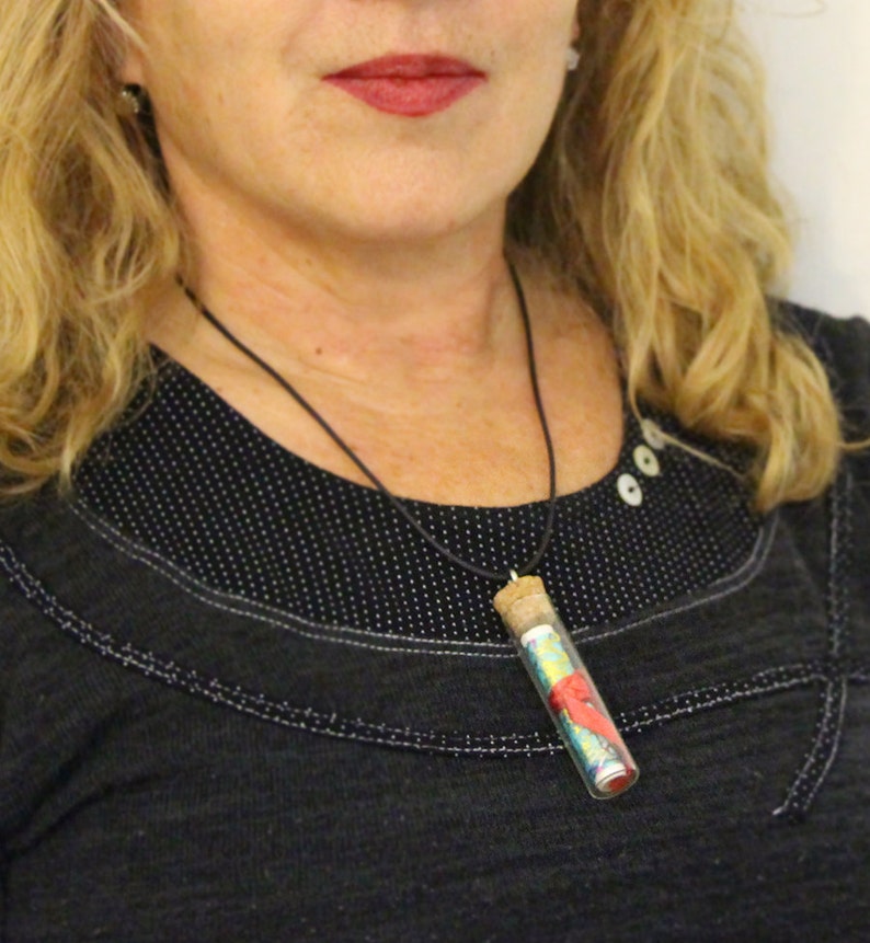 May include: A black necklace with a small glass vial pendant filled with colourful fabric scraps. The vial has a cork stopper and is hanging from a black cord.