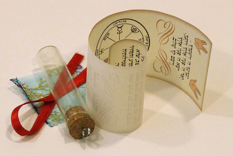 May include: A rolled up scroll with Hebrew text and a circular design. The scroll is tied with a red ribbon and a glass vial with a cork stopper.