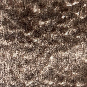 May include: Close-up of a textured fabric in shades of brown and tan. The material has a plush, velvety appearance with a slightly uneven surface, creating a play of light and shadow. The fabric's texture suggests it could be used for upholstery or apparel.