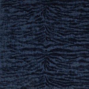 May include: Close-up of a navy blue fabric with a textured surface. The fabric features a repeating pattern of stylized, organic shapes in a darker shade of blue, creating a subtle contrast and visual interest. The overall effect is a rich, luxurious textile.