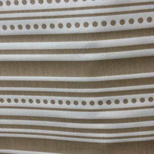 May include: Close-up of a fabric with a repeating pattern of horizontal stripes and dotted lines. The stripes and dots are a warm brown color, while the background is a lighter beige. The fabric has a textured appearance.