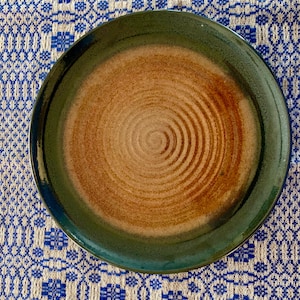 May include: A large, round ceramic plate with a green rim and a brown center. The center of the plate has a swirling pattern.
