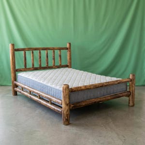 May include: A bed frame constructed from dark brown, rounded logs featuring a headboard with vertical slats and a footboard. The frame supports a thick, white mattress with a quilted, diamond-patterned surface and gray side panels.