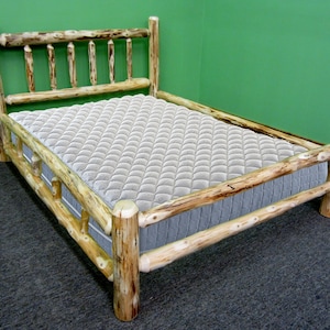 May include: A rustic wooden bed frame with a light-colored mattress. The bed frame is constructed from natural logs, featuring a headboard with vertical supports and a footboard. The mattress is a neutral color, providing a contrast to the wood.