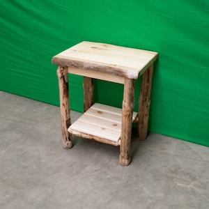 May include: A rustic wooden end table with a natural wood finish. The table has a single shelf and is made from rough-hewn logs.