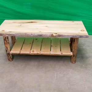 May include: A rustic wooden coffee table with a natural wood finish. The table has a single shelf and is made from rough-hewn logs.