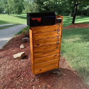 May include: A wooden mailbox post with a black mailbox and the house number 2532. The mailbox is mounted on the post and has a red flag.