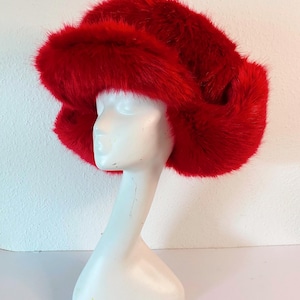 May include: A bright red faux fur hat with a wide brim and ear flaps. The hat is made of soft, fluffy material and has a classic trapper style.