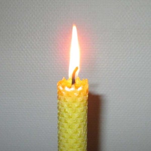 May include: A yellow beeswax candle with a honeycomb pattern is lit and burning. The flame is a bright orange and yellow.