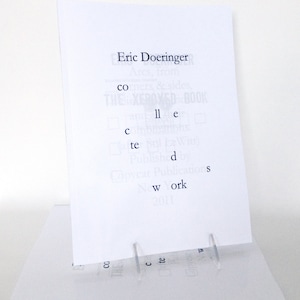 May include: A white book cover with the title "Collected Works" and the author's name "Eric Doeringer". The book cover also includes the text "Copycar Publications" and "New York 2011".