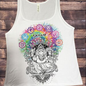 May include: White tank top with a colorful tie-dye design featuring a black and white illustration of Ganesha, the Hindu god of wisdom and prosperity. The design also includes the word "Namaste" and seven chakras.