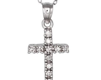 May include: A silver-toned metal necklace featuring a delicate chain and a cross pendant. The cross is embedded with multiple small, clear, sparkling stones arranged along its vertical and horizontal bars, suspended from a simple metal bail.