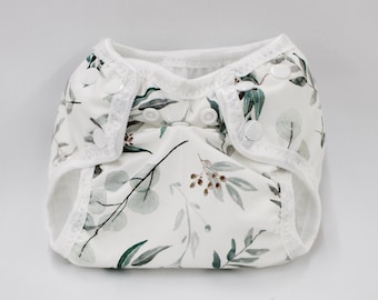 May include: A white cloth diaper with a floral print featuring green leaves and brown berries. The diaper has a white lace trim around the edges.