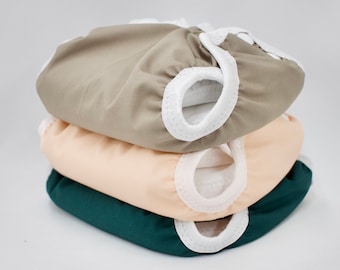 May include: Three reusable cloth diapers in different colors: a light brown diaper, a peach-colored diaper, and a dark green diaper. Each diaper has a white elastic trim around the edges.