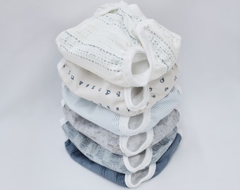 May include: A stack of six reusable cloth diapers in various blue and white patterns. The diapers are folded and stacked on top of each other. The top diaper has a white background with a light blue and gray pattern.