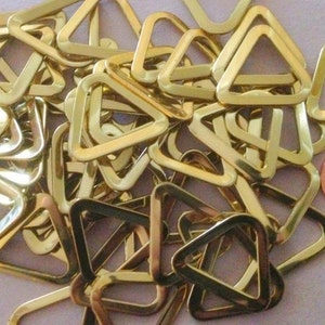 May include: A collection of shiny, gold-colored triangle rings. The rings are made of metal and appear to be new. A copper penny is included for size comparison. These rings could be used for various craft or jewelry projects.