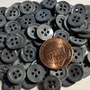 May include: A pile of gray plastic buttons with four holes each. A US penny is included for scale.