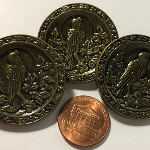 May include: Three antique gold-toned metal buttons with a raised design of a bird in a leafy setting. The buttons are approximately the size of a US penny.