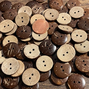 May include: A pile of brown and natural coconut shell buttons. The buttons are round and have two holes. A US penny is included for scale.