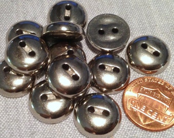 May include: A group of 10 silver metal buttons with two holes each. The buttons are about the size of a US penny.