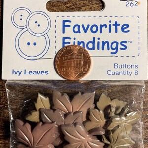 May include: A package of eight ivy leaf-shaped buttons in shades of brown and tan. The package is labeled "Favorite Findings" and includes a penny for size comparison.