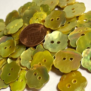 May include: A large pile of yellow, iridescent, flower-shaped buttons. The buttons have two holes and are approximately the size of a US penny.