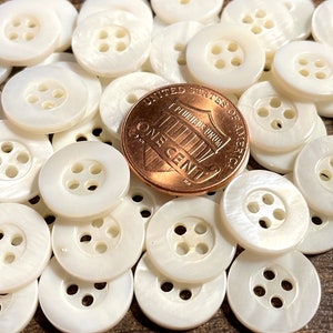 May include: A pile of white, round, four-hole buttons made of mother of pearl. A US penny is included for scale.