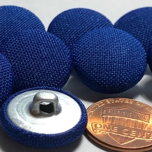 May include: Six blue fabric buttons with a silver shank. The buttons are approximately the size of a US penny.