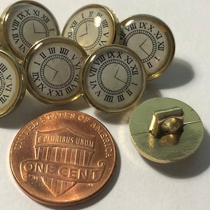 May include: Six gold-toned clock face buttons with Roman numeral markings. The buttons have a raised edge and a flat back. One button is shown with a gold-toned shank on the back.