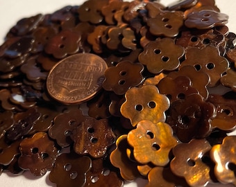 May include: A pile of brown, iridescent, flower-shaped buttons with two holes each. A US penny is included for scale.