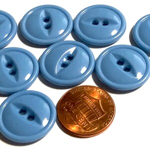 May include: Ten light blue plastic buttons with two holes each. The buttons have a slightly raised, rounded design. A penny is included for size comparison.