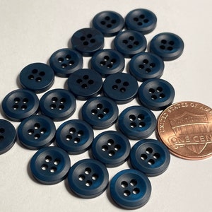 May include: A group of 20 dark blue plastic buttons with five holes each. The buttons are arranged in a semi-circle with a penny for scale.