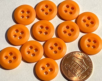 May include: A collection of ten orange plastic buttons with four holes each. The buttons are arranged in a circle around a US penny.