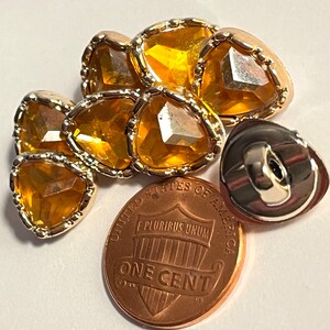 May include: Six gold-rimmed, amber-colored, triangular buttons with a single silver-toned button on the right. The buttons are arranged in a semi-circle and are about the size of a US penny.