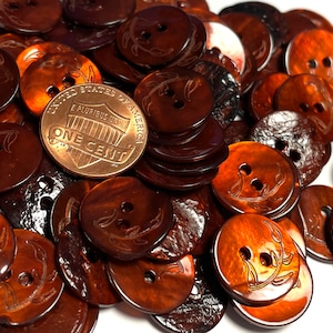 May include: A pile of brown, round, two-hole buttons with a leaf design. The buttons are made of a shiny, iridescent material.  The text "UNITED STATES OF AMERICA E PLURIBUS UNUM ONE CENT" is visible on a copper penny.