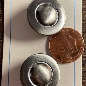 May include: Two silver metal buttons with a raised center, displayed on a white card with blue trim. The card also features the text "BGE...first in fashion" and "80¢".