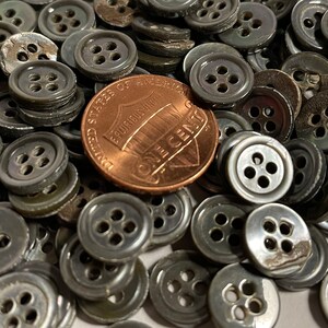 May include: A large pile of gray, four-hole buttons, with a US penny for scale.
