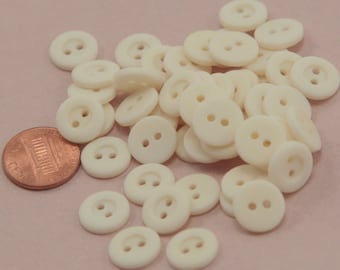 May include: A pile of off-white plastic buttons with two holes each. The buttons are arranged in a random pattern and are all the same size.