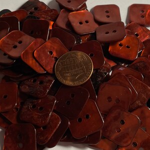 May include: A pile of 50 brown, square-shaped buttons with two holes each. The buttons have a shiny, iridescent finish.
